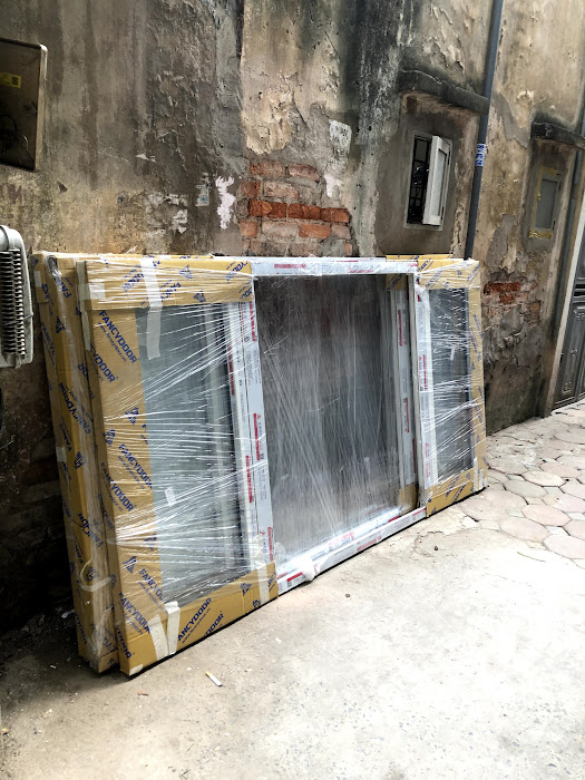 Cửa nhôm kính Xingfa mới bọc nilon đặt tựa tường ngoài trời chuẩn bị lắp đặt